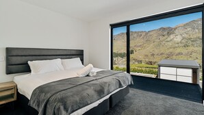 Une chambre moderne avec un grand lit, une table de chevet et une vue sur un paysage montagneux par une grande fenêtre.