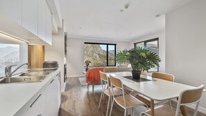 Une cuisine moderne avec des meubles blancs, un coin repas doté d’une table et de chaises blanches, et une grande fenêtre offrant une vue sur les montagnes.