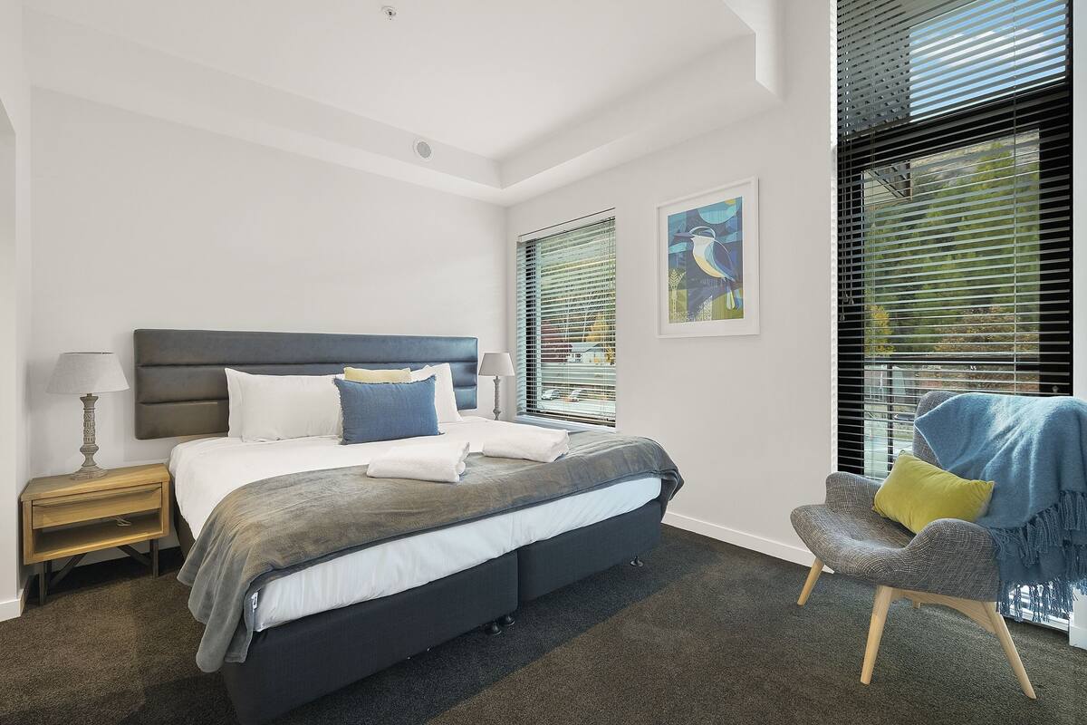 Un dormitorio moderno con una cama grande, mesitas de noche, una silla y obras de arte en las paredes.