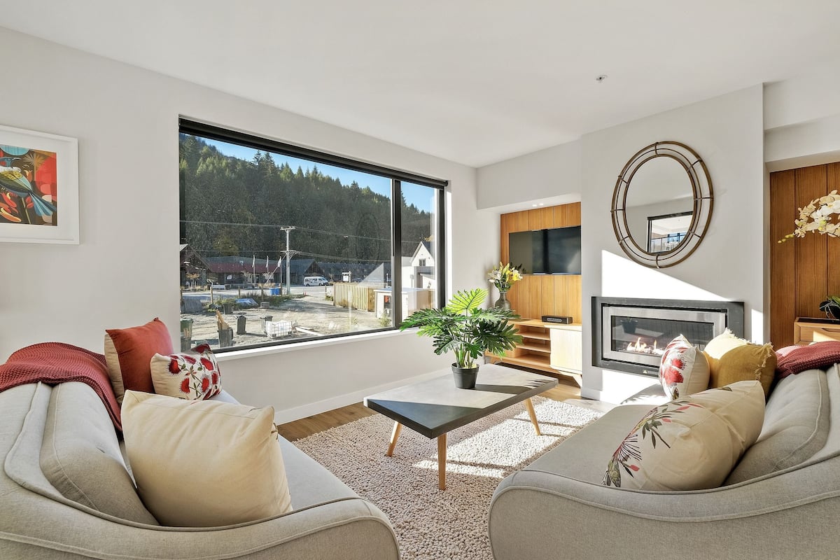 Una sala de estar moderna con un ventanal grande, una chimenea y un área de descanso confortable.