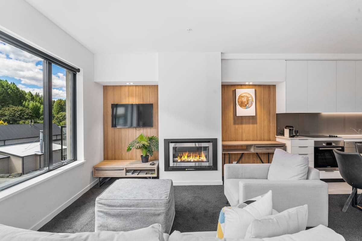 Una sala de estar moderna con chimenea, televisión de pantalla plana y comedor, con cocina al fondo.