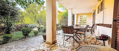 Un patio al aire libre techado con suelo de piedra, mobiliario de mimbre y vistas a zonas verdes.