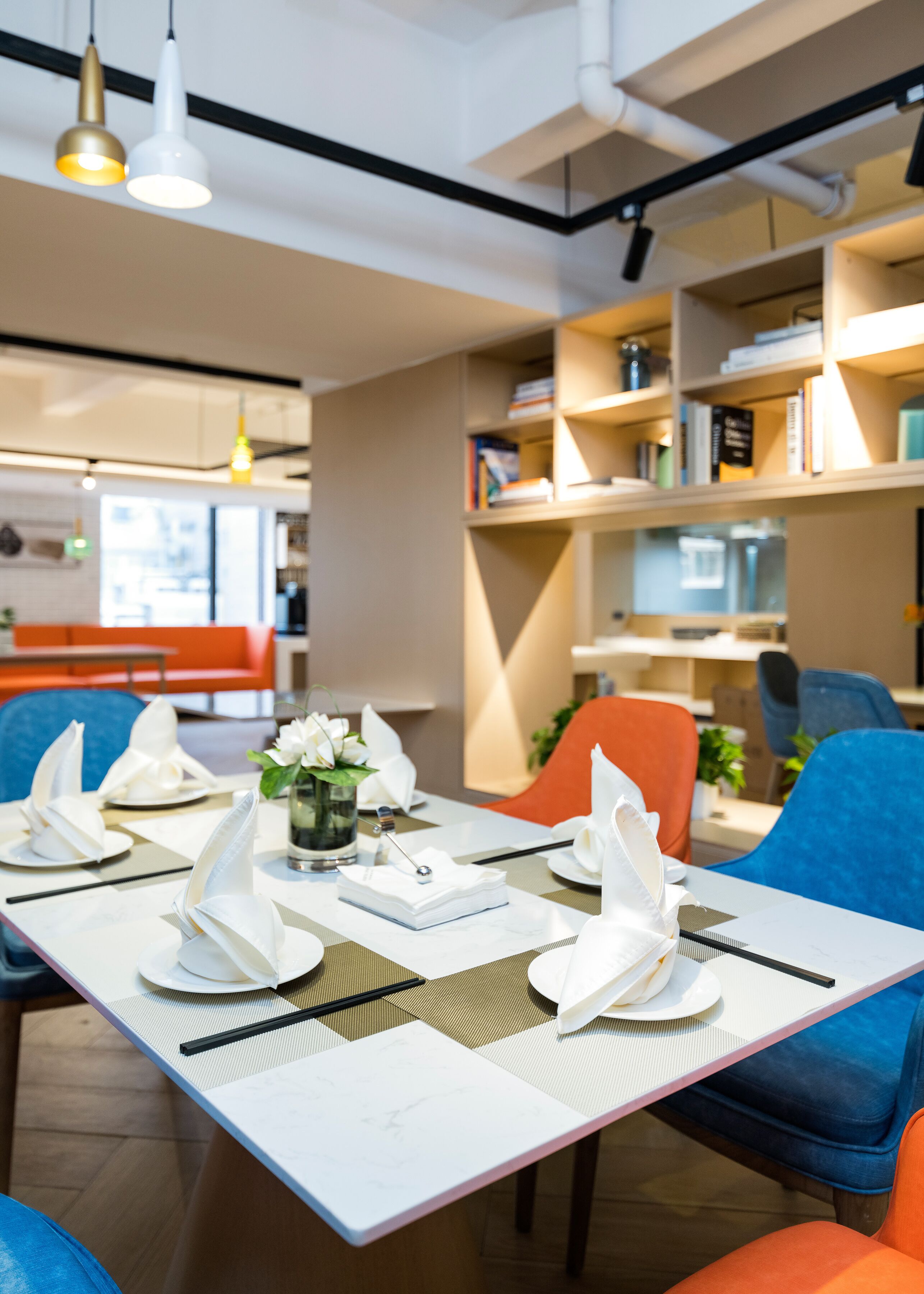 Un comedor moderno con una mesa blanca dispuesta para cuatro personas, sillas azules y una estantería al fondo.