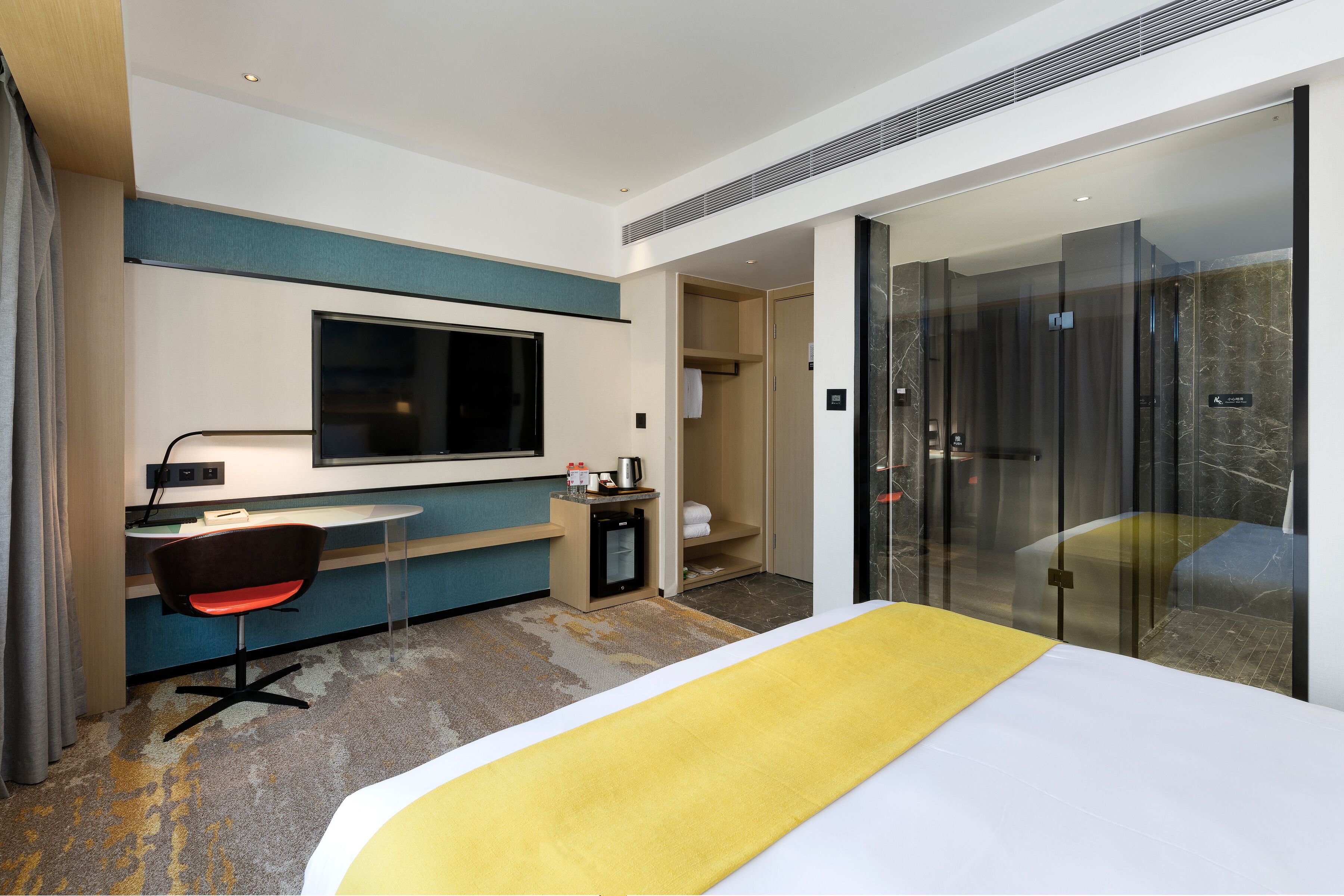 Una camera d'albergo moderna con un letto, una scrivania con una sedia, una televisione e un box doccia in vetro.