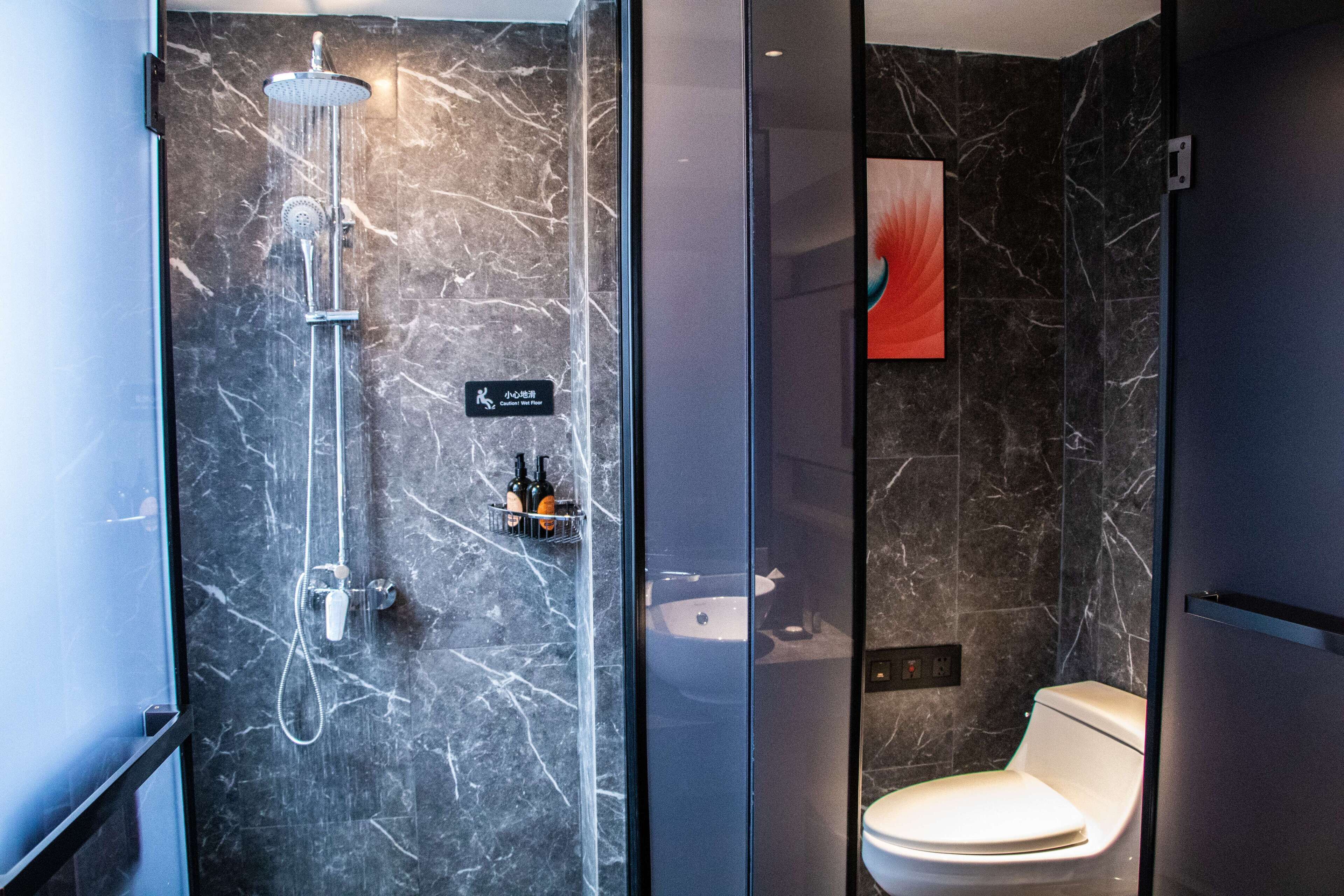 Un baño moderno con cabina de ducha de vidrio, un inodoro y pared de mármol.