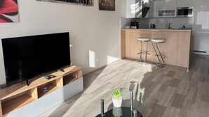 A modern kitchen with a central island, bar stools, and a flat-screen TV on a wooden stand. - Spacious 2BR + balcony in Prague I Comfort & Style. (Praha 9)