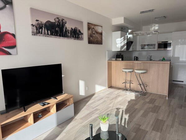Una cocina moderna con una isla central, taburetes de bar y un televisor de pantalla plana sobre un soporte de madera.
