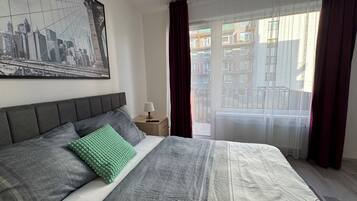 A neatly made bed with a grey and white duvet, a green pillow, and a cityscape artwork on the wall.