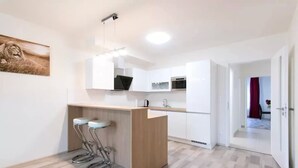 A modern kitchen with white cabinets, a wooden countertop, and two bar stools. - Spacious 2BR + balcony in Prague I Comfort & Style. (Praha 9)
