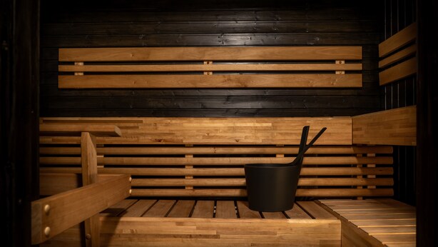 A sauna with wooden benches and a black container, likely for water or oil. - Motelli Online Oy (Porvoo)