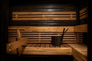A sauna with wooden benches and a black container, likely for water or oil. - Motelli Online Oy (Porvoo)