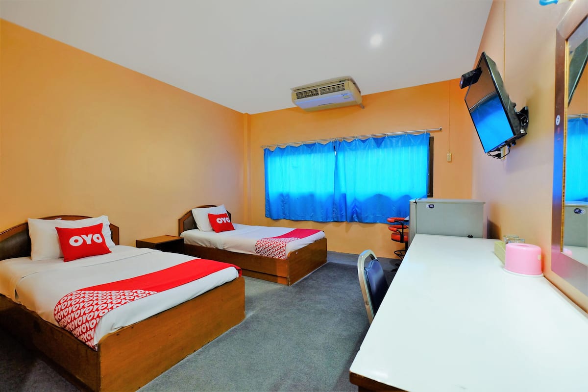 A hotel room with two beds, a desk, a television, and an air conditioning unit.