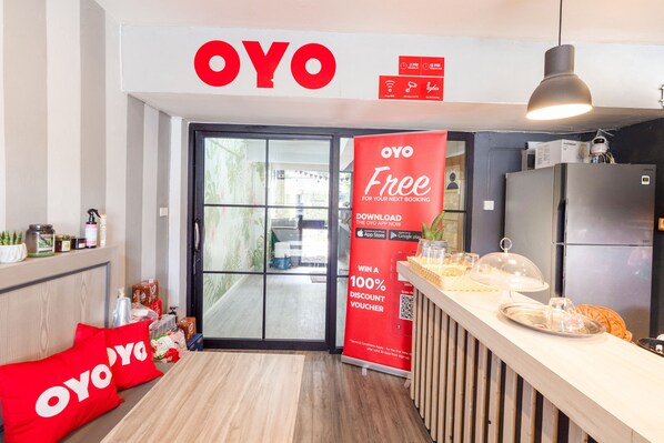 A modern kitchen with a refrigerator, a sink, and a wooden countertop. There is a large OYO sign above the door and a promotional banner for the OYO app.