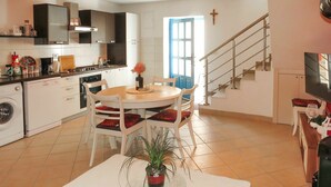 Une cuisine moderne avec des meubles blancs, une table à manger avec des chaises, un lave-linge et un escalier menant à un palier.