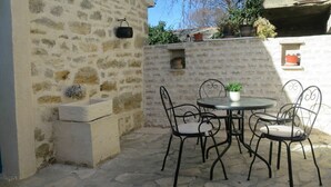 Une terrasse en pierre avec une table ronde et quatre chaises.