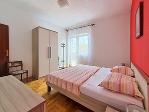 Um quarto com cama, cadeira, guarda-roupa e janela com cortinas.