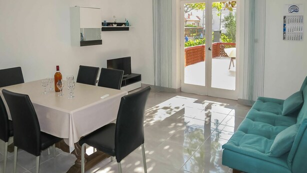 Ein moderner Essbereich mit einem Tisch für vier Personen, einer Couch und einer Schiebeglastür, die auf eine Terrasse im Freien führt.