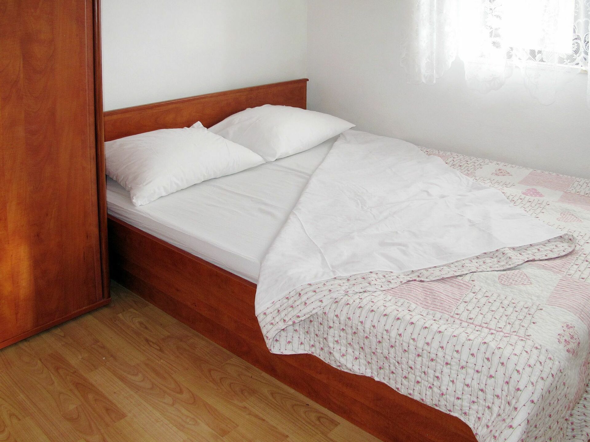 Un lit simple avec une literie blanche et une couverture à motifs floraux, une tête de lit en bois et un plancher en bois.