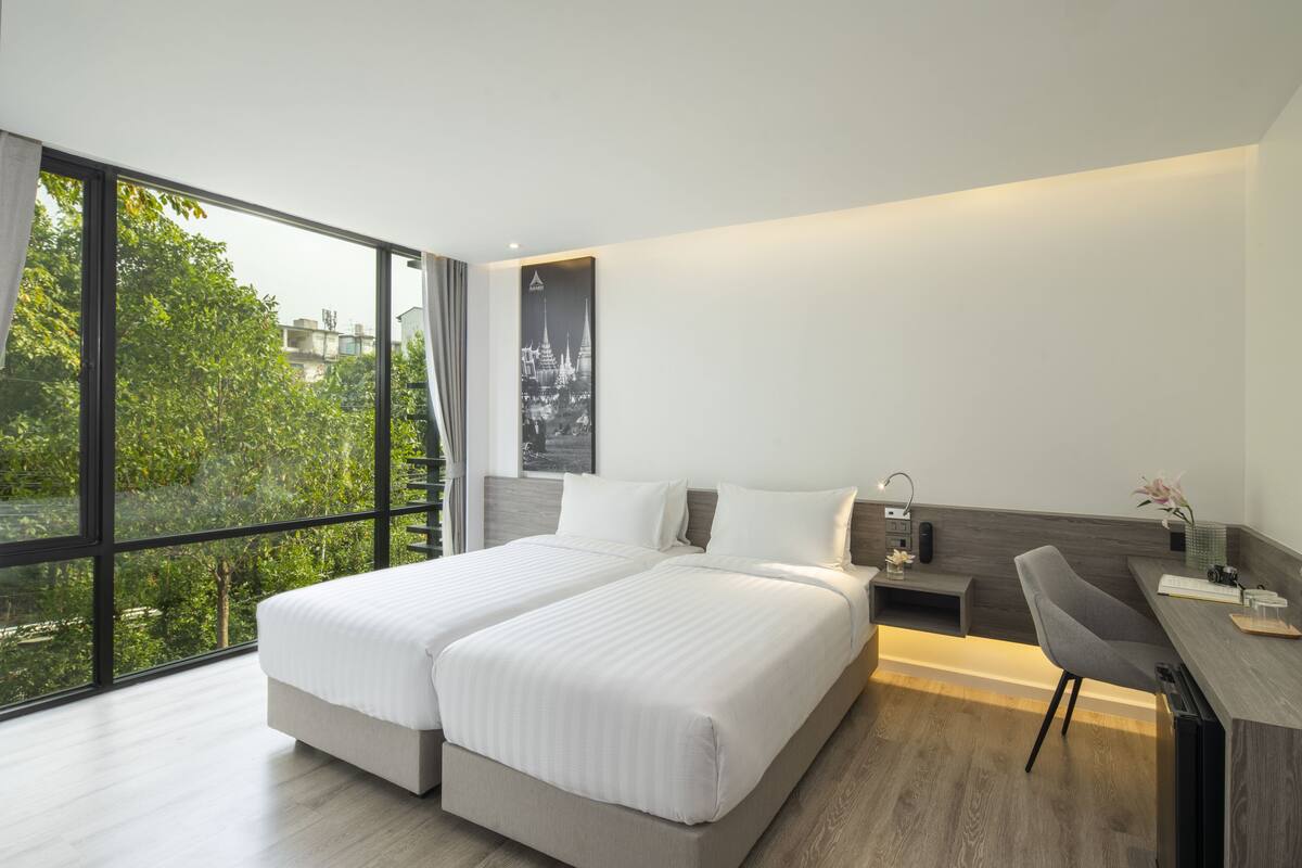 A modern hotel room with a large bed, a desk, and a view of greenery outside.