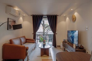 Un salon moderne avec un canapé, une table basse, un téléviseur et un balcon agrémenté de rideaux.