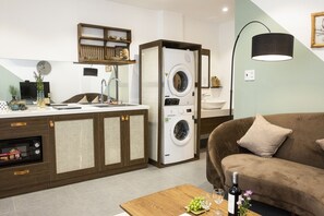 Een ruimtelijke woonkamer met een kitchenette, een wasmachine, een bank en een eettafel met een fles en glazen.