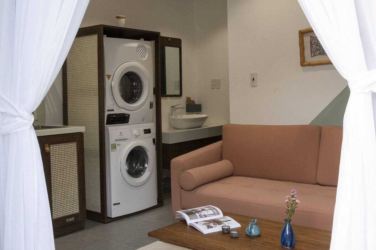 A compact living space with a washing machine, a sofa, a coffee table, and a small bathroom area.