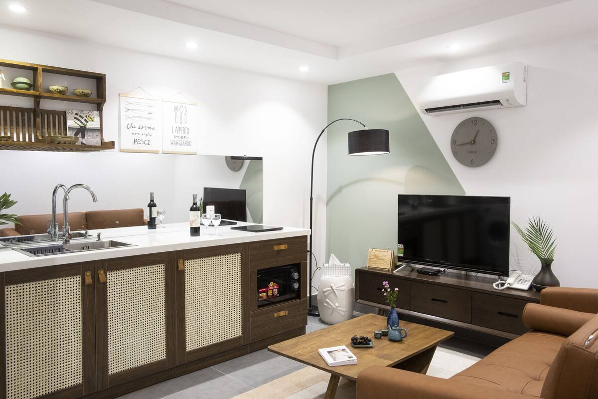 A modern kitchen with a sink, countertop, and cabinets. There is a television, a clock, and a plant on the wall.