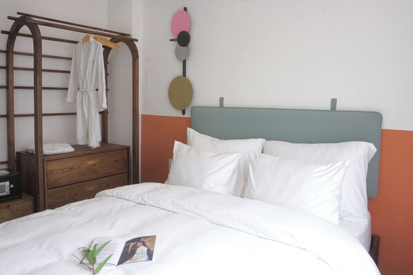 A neatly made bed with white bedding, a wooden dresser with a towel hanging on it, and a wall-mounted towel rack.