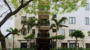Un edificio de varios pisos con entrada central, balcones y plantas en macetas.