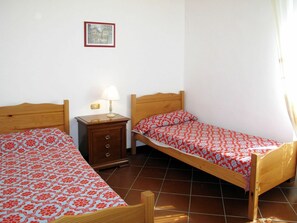 A small, clean room with two wooden beds, a nightstand with a lamp, and a framed picture on the wall. - Beautiful private villa for 5 guests with pool, TV, terrace and pets allowed (Dolcedo)