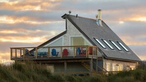 A beach house with a sloped roof, a balcony with colorful Adirondack chairs, and a view of the beach.