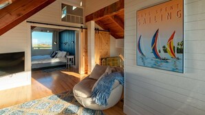 A cozy loft bedroom with a large bed, a seating area with a bean bag, and a view of the outdoors.