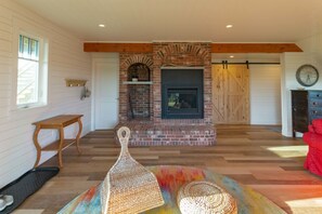 A cozy living room with a brick fireplace, wooden beams, a red couch, and a colorful rug.