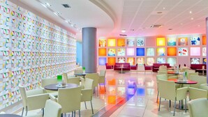 Un intérieur moderne avec un mur orné de motifs géométriques colorés, une colonne centrale et un espace détente comprenant des tables et des chaises.