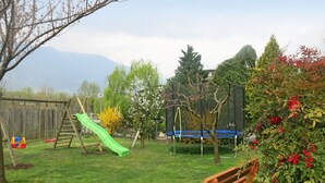 Un patio trasero con un tobogán de madera, un columpio, un trampolín y un banco de madera.