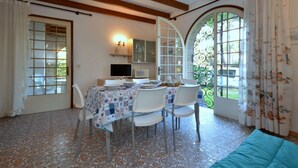 Un coin repas avec un sol carrelé, une table dressée pour quatre personnes et un téléviseur en arrière-plan.