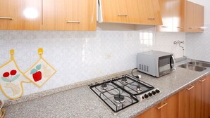 A kitchen with wooden cabinets, a gas stove, a microwave, and a stainless steel sink. - Beautiful  villa for 6 people with A/C, TV, terrace and pets allowed (Lignano Sabbiadoro)