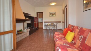A living room with a sofa, a dining table with chairs, a kitchen area, and a staircase. - Beautiful  villa for 6 people with A/C, TV, terrace and pets allowed (Lignano Sabbiadoro)