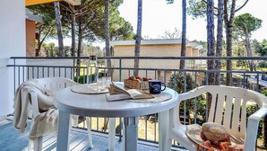 A balcony with a table set for two, a chair, and a view of trees and buildings. - Lovely apartment for 8 guests with A/C, TV, terrace and pets allowed (San Michele Al Tagliamento)
