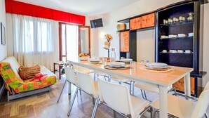 A dining area with a long table, white chairs, and a buffet-style cabinet with glassware. - Lovely apartment for 8 guests with A/C, TV, terrace and pets allowed (San Michele Al Tagliamento)