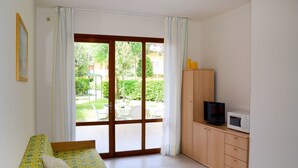 A room with a bed, a TV, a microwave, and a view of a garden through a sliding door. - Lovely apartment for 6 guests with A/C, TV, terrace and pets allowed (San Michele Al Tagliamento)