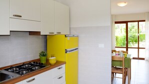 A kitchen with white cabinets, a yellow refrigerator, a gas stove, and a dining area with a table and chairs. - Lovely apartment for 6 guests with A/C, TV, terrace and pets allowed (San Michele Al Tagliamento)