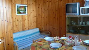 A wooden-paneled room with a sofa, a dining table set with plates, glasses, and cutlery, and a television on a shelf. - Wonderful  villa for 8 people with A/C, TV, terrace and pets allowed (San Michele Al Tagliamento)