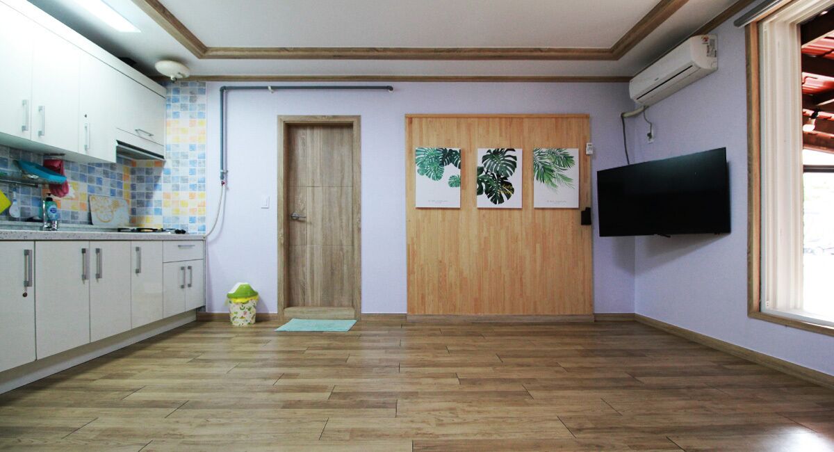 A kitchen with wooden cabinets, a tiled backsplash, a wooden door, and a mounted TV.