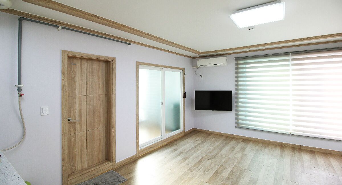 Habitació amb sòl de fusta, porta corredissa de vidre, televisió penjada a la paret i finestra amb persianes.