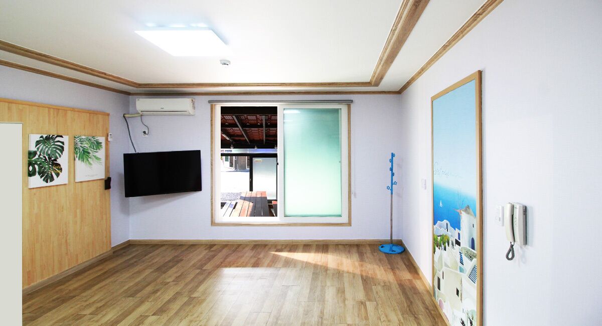 Une pièce dotée d’un plancher en bois, d’un téléviseur à écran plat fixé au mur, d’une fenêtre donnant sur l’extérieur et d’une porte ornée d’un panneau décoratif.