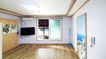 Une pièce dotée d’un plancher en bois, d’un téléviseur à écran plat fixé au mur, d’une fenêtre donnant sur l’extérieur et d’une porte ornée d’un panneau décoratif.