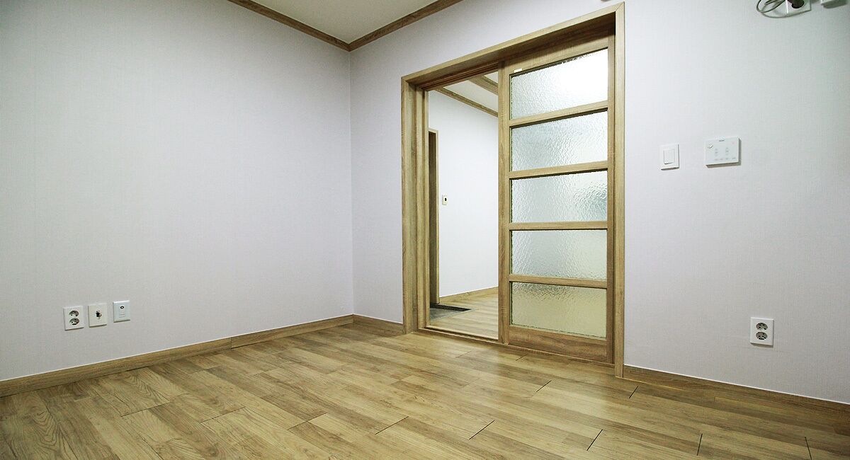 Una habitació amb terres de fusta, una porta corredissa de vidre i parets blanques.
