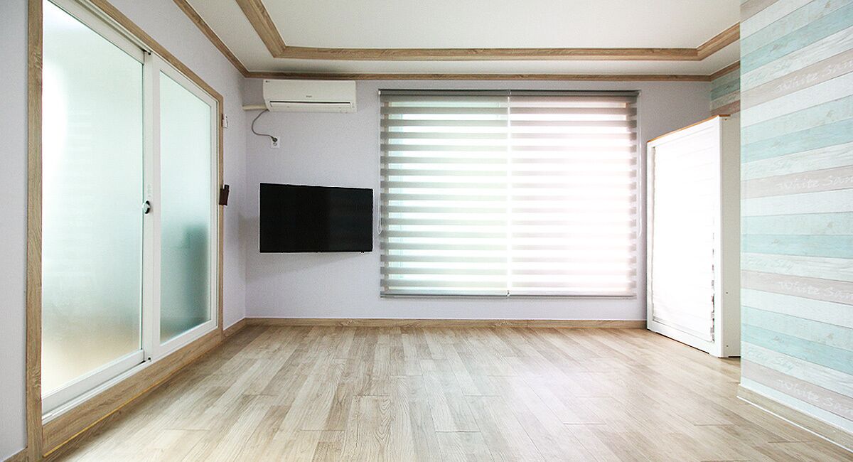 A room with a large window, a flat-screen TV mounted on the wall, and a wooden floor.