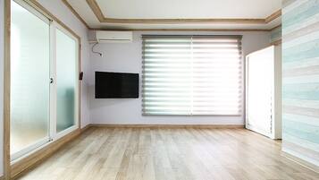 A room with a large window, a flat-screen TV mounted on the wall, and a wooden floor.